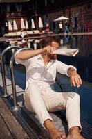 Covering himself by newspaper from bright, sunlight. Handsome man in formal clothes is in the pool photo