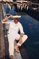 Covering himself by newspaper, from bright sunlight. Handsome man in formal clothes is in the pool photo