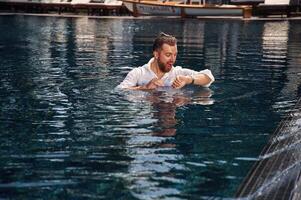 Checking the time, in the water. Handsome man in formal clothes is in the pool photo