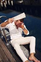 Holding ,newspaper. .Handsome man in formal clothes is in the pool photo