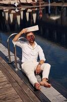 Covering, himself b,y newspaper from bright sunlight. Handsome man in formal clothes is in the pool photo