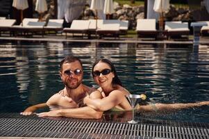 In sunglasses, smiling,. Man ,with woman is in the pool together photo