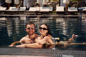 In sunglasses, smiling,. Man with ,woman is in the pool together photo