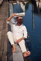Covering himself, by newspaper from bright sunlight. Handsome man in formal clothes is in the pool photo