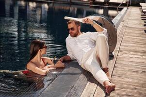 With newspaper in hand.. Man ,with woman is in the pool together photo