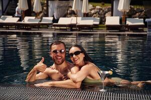 In sunglasses,, smiling. Man with, woman is in the pool together photo