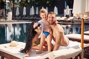 Posing ,and ,smiling. Happy family of father, mother and son are in the pool photo