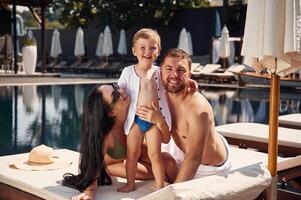 Posing and, smiling. Happy family of father, mother and son are in the pool photo