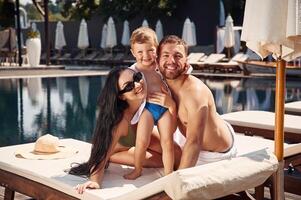 Posing and smiling.. Happy family of father, mother and son are in the pool photo