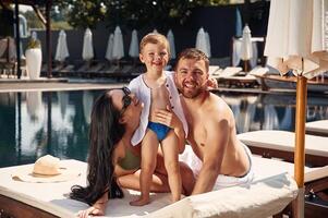 Posing and smiling. Happy, family of father, mother and son are in the pool photo