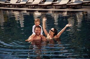 In the water... Happy family of father, mother and son are in the pool photo