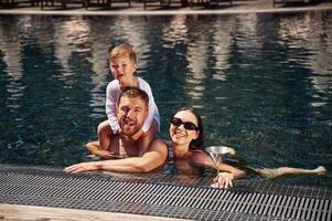 Front view. Happy family, of father, mother and son are in the pool photo