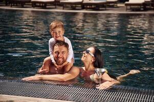 Smiling, having fun. Happy, family of father, mother and son are in the pool photo