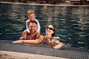 Smiling, having fun. Happy family of, father, mother and son are in the pool photo