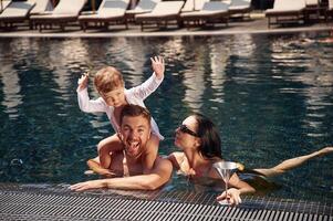 Front view. Happy family of, father, mother and son are in the pool photo