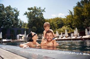 Boy, is sitting on man shoulders. Happy family of father, mother and son are in the pool photo