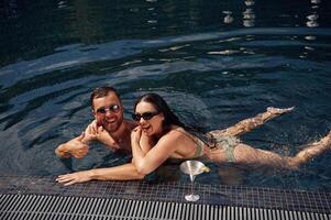 In ,sunglasses, smiling. Man with woman is in the pool together photo