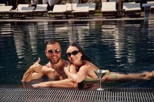 In sunglasses,, smiling. Man with woman is in the pool together photo