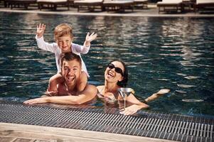 Smiling,, having fun. Happy family of father, mother and son are in the pool photo
