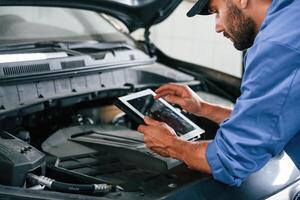 With, tablet in hands.. Auto ,mechanic working in garage. Repair service photo