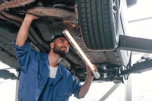 Under car, using lighting, device. Auto mechanic working in garage. Repair service photo
