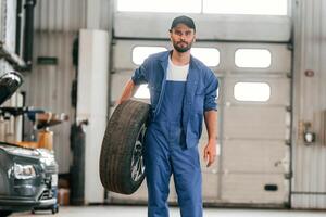 Front view, standing, and holding, tire. Auto mechanic working in garage. Repair service photo