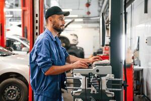 Standing by computer ,terminal. Auto mechanic working in garage. Repair service photo