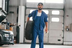 Front view, standing and holding, tire. Auto mechanic working in garage. Repair service photo