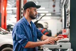 In black cap. Using computer., Auto mechanic working in garage. Repair service photo