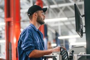 In black cap. Using computer. Auto ,mechanic working in garage. Repair service photo