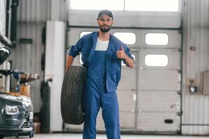 Front ,view, standing and holding tire. Auto mechanic working in garage. Repair service photo