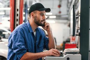 In black, cap. Using computer. Auto mechanic working in garage. Repair service photo