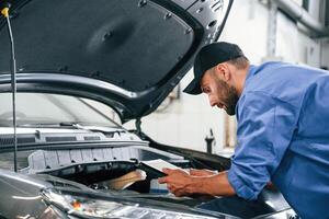 With tablet in hands.. Auto mechanic working in garage. Repair service photo