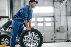 New tire, moving it. Auto mechanic working in garage. Repair service photo