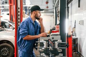 Standing by, computer terminal. Auto mechanic working in garage. Repair service photo
