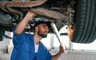 Standing under a car. .Auto mechanic working in garage. Repair service photo