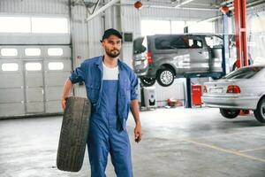 Walking ,forward with new tire. Auto mechanic working in garage. Repair service photo