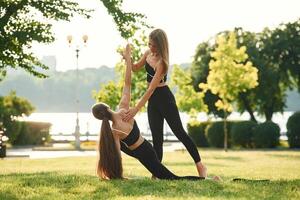 Teaching, how to, do ,exercises. Two ,women in sport clothes are doing exercises outdoors on the field photo