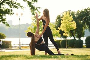Teaching how, to do exercises.. Two ,women in sport clothes are doing exercises outdoors on the field photo