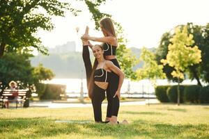 Professional trainer ,is helping. Two, women in sport clothes are doing exercises outdoors on the field photo
