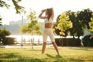 White,, sportive clothes. Beautiful young woman is in the park at sunny daytime photo