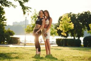 Standing ,and, posing. Two women in sport clothes are doing exercises outdoors on the field photo