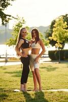 Looking to, the camera. Two women in sport clothes are doing exercises outdoors on the field photo