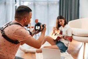 Photographer is ,working, using camera. Beautiful woman in casual clothes is at home with guitar photo