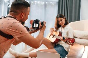 Photographer ,is working, using camera. Beautiful woman in casual clothes is at home with guitar photo