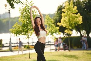Raising the hands up. Beautiful young ,woman in sportive clothes is in the park at sunny daytime photo