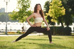 Exercise for ,legs stretching. Beautiful ,young woman in sportive clothes is in the park at sunny daytime photo
