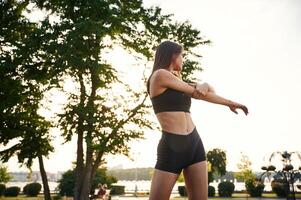 Exercises,, against, tree and sky. Beautiful young woman in sportive clothes is in the park at sunny daytime photo
