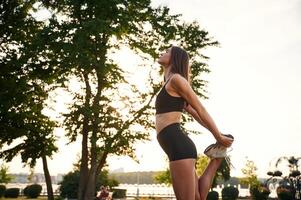 Exercises, ,against tree and sky. Beautiful young woman in sportive clothes is in the park at sunny daytime photo