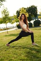 Doing fitness... Beautiful young woman in sportive clothes is in the park at sunny daytime photo